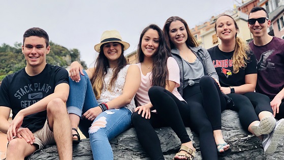Six smiling students seated on a rock